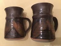 Two pottery mugs by Robin Hopper with dark mottled glaze and handles, similar size shown.