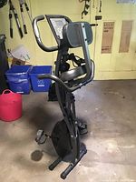 Side view of Slim Cycle exercise bike folded upright, showing padded seat, backrest, arm resistance bands, and pedals.