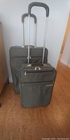 Photo showing two olive green Briggs & Riley roller-ball luggage pieces with extended handles, standing upright.