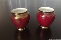 Two deep red ceramic CarltonWare vases with gold trim, shown side by side on dark surface