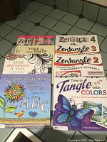 Eight Zentangle books arranged on the floor including Zen Doodle Workbook, Yoga for Your Brain, One Zentangle A Day, Zenspirations ABC, Zentangle 2, 3, 4, and Time to Tangle with Colors.