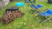 Photo showing two blue folding deck chairs, a small blue kiddie pool with paint area, a black item, and several bamboo yard art pieces piled on grass.