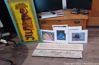 Five unframed art pieces on floor including tall African-themed yellow background art, two long wood banners with phrases, and three smaller art prints featuring Georgia O'Keeffe images.