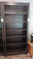 Full view of tall dark brown bookshelf with five shelves