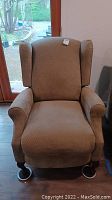 Front view of the brown upholstered reclining chair showing padded armrests and high wingback style backrest.