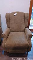 Front view of brown fabric reclining armchair showing upholstery and tag on backrest.