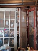Two antique wooden doors with multiple glass panes, worn condition, leaning against wall in storage area