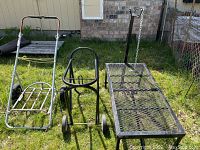 Three items displayed outside on grass: metal cart with mesh top and chain, black wheeled saddle stand, and metal goat stand with neck brace.