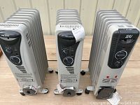 Three oil-filled radiator heaters side by side with visible brand logos and manual dials on front.