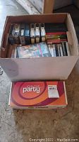 Box filled with assorted media cases including VHS tapes and DVDs.