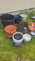 Image showing seven garden pots of varying sizes and materials on grass, some on wooden pallets.