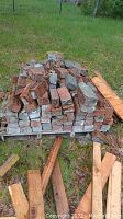 Stacked used bricks on pallets outdoors with scrap wood pieces scattered nearby.