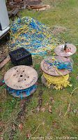 View of three wooden reels with synthetic rope and a large pile of mixed colored rope on ground outside
