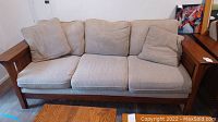 Full view of beige fabric sofa with three seat cushions and wooden armrests