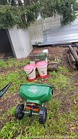 Photo showing Scott's Turf Builder Seed Spreader, two Harris Farm poultry drinkers and stacked concrete blocks with other materials