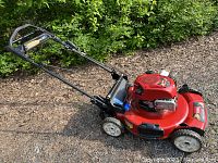 Side view of Toro lawn mower showing red deck, engine, self-propelled handle, grass catcher attachment.