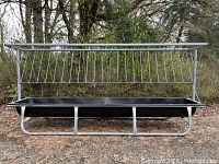 Front view of galvanized steel hay feeder frame with attached black plastic trough resting outdoors on ground