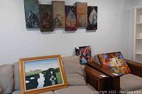 Overall view of wall art items including leaf wall art atop sofa and framed cow painting leaning on sofa, plus two abstract paintings on armrests.
