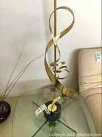 Brass ribbon sculpture with looping and spiral forms on a round black stone base.
