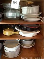 Shelves with stacked white ceramic dishes with stripe pattern, clear glass dishes, and colored cookware including yellow and white ceramic pots with lids.