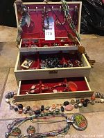 Jewelry box opened showing multiple compartments filled with various costume jewelry including chunky necklaces and rings