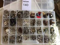 Full view of plastic organizer box filled with various silver tone necklaces and earrings in multiple compartments.