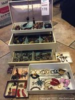 Full view of white multi-tier jewelry box with various costume jewelry in compartments and trays.