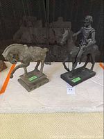 Two statues on a table: a metal horseman on horse about 17 inches tall and a cement horse on base.