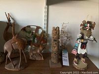 Shelf display of wooden animal carvings, woven basket, totem pole sculpture, Kachina doll, and pottery with dried flowers.