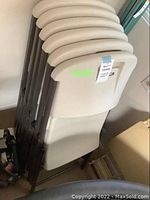Stack of six Lifetime folding chairs showing beige plastic backrests and seats, brown metal frames folded flat