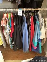 Photo showing assorted ladies tops and jackets on hangers, various colors including reds, blues, pastels.