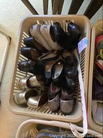 View of five pairs of ladies shoes in plastic basket, showing black, beige, silver, and gray shoes.