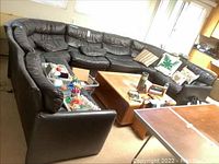 Front and side view of black leather sectional sofa with coffee table and various items around.