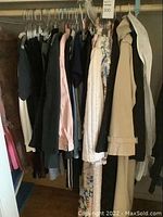 Closet rack showing multiple items of ladies clothing including coats, dresses, and nightgowns in various colors mostly neutral and pastel shades.