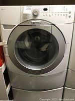 Front view of Maytag washer showing electronic control panel, round door and storage pedestal drawer