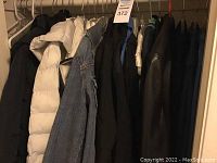 Closet view with multiple jackets and coats hanging on a rod, including white puffer, dark coats, and denim jacket