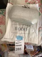 Silver textured Rodo handbag resting on white dust cover with Rodo brand and made in Italy text visible