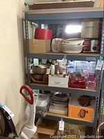 Metal utility shelving unit with four shelves, shown with various items on shelves for scale and size reference but lot includes no contents.