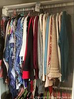 Full view of the clothing rack showing various jackets and blouses on hangers with different fabrics and prints.