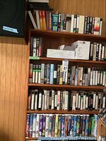 Wide view of multiple wooden shelves holding many VHS tapes neatly organized with some boxes on top.