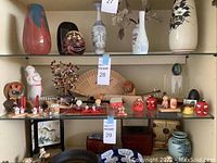 Shelf view of multiple small Asian-inspired decor items including figurines of children, animals, fans, and vases