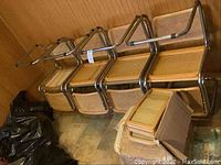 Seven chrome-frame cane-seat chairs leaning against wall, spare cane backs in box on floor
