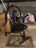 Side view of the Ab-Doer Pro exercise bench showing curved blue padded handles, resistance bands attached to vertical bar, and black padded seat with logo.