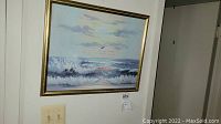 Framed seascape painting on wall showing waves and sky with light switch nearby