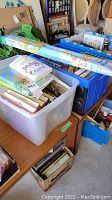 Plastic bins filled with assorted books and several rolled laminated world maps on top.