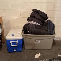 View of the cooler and bin filled with sleeping bags and a blanket in a basement setting against a concrete block wall.