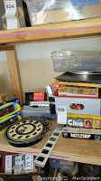 View of multiple board games stacked including Clue, Battleship, and Stand Up along with plastic pool balls and a plastic container with small items.