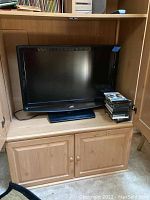 JVC 31 inch flat screen TV placed on wooden shelf, showing front view of TV and base stand with DVDs stacked to the right side.