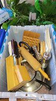 Photo of kitchen utensils including wooden rolling pin, knife block with knives, metal pots and cutting boards in plastic bin.