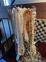 Ornate metal necklace stand holding multiple costume necklaces including faux pearls and multi colored beads.
